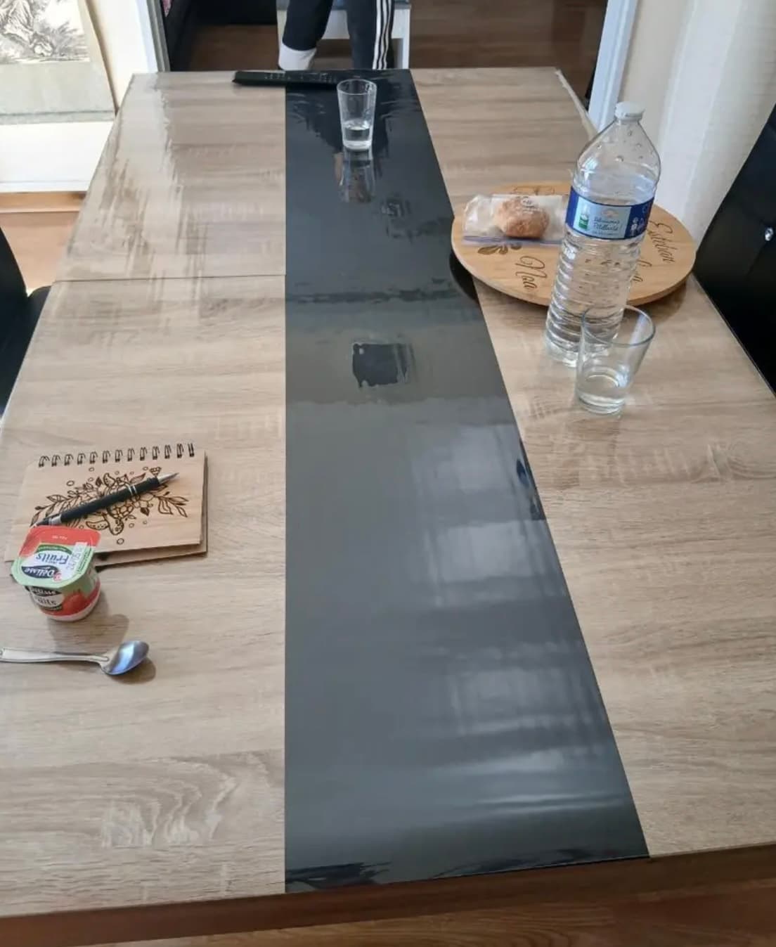 Raňajky na dlhom stole s grafitovým pruhom: voda, poháre, zápisník - všetko na podložke