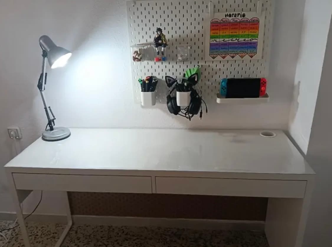 Biely písací stôl s lampou a doskou na stenu; vrchná časť je chránená priehľadným krytom